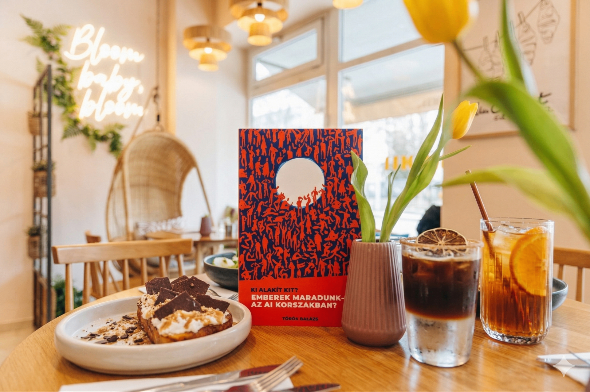 A könyv egy világos kávézóasztalon, tulipánokkal és hideg kávéval: nyugodt olvasási helyzet egy nyugtalan témához.